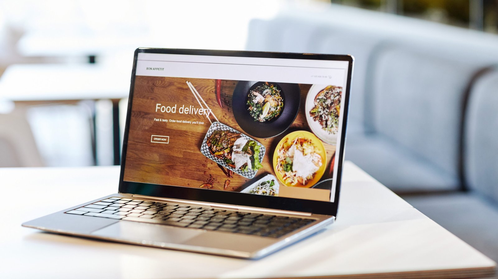 Background image of opened laptop with Food delivery website on table in food court or cafe interior, copy space