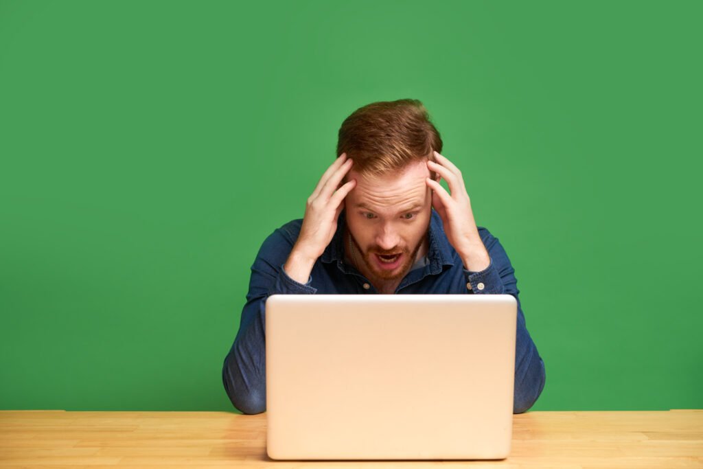 Shocked young redhead businessman in shirt holding head in hands and reading internet news on laptop