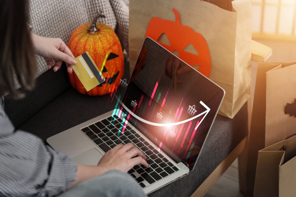 Customer making an online payment on a laptop surrounded by Halloween pumpkin decorations and paper shopping bags.